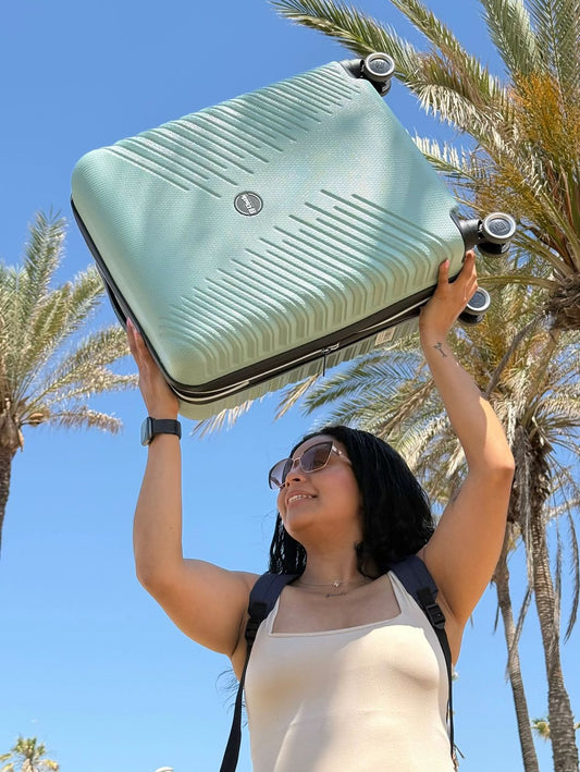 Mujer sosteniendo la Maleta de Cabina Gaza de Unikrevolution bajo un cielo azul con palmeras